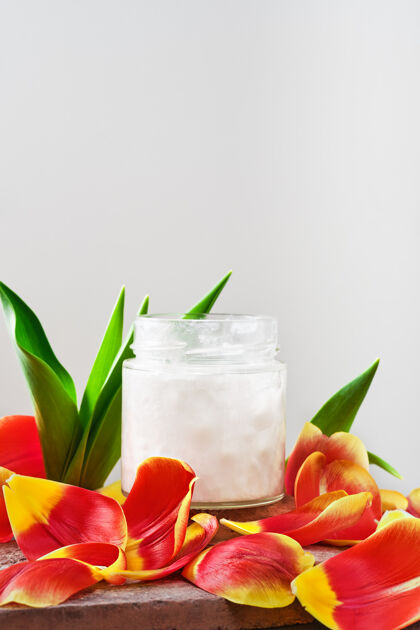 椰子椰子油在白色的罐子里被郁金香花瓣包围 特写有临摹空间替代品可可芳香疗法