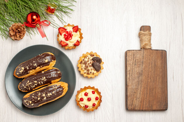 餐厅俯瞰图：灰色盘子上的巧克力蛋糕装饰着松树叶子 左边是圣诞玩具 右边是白色木质地面上的砧板食物树叶木头