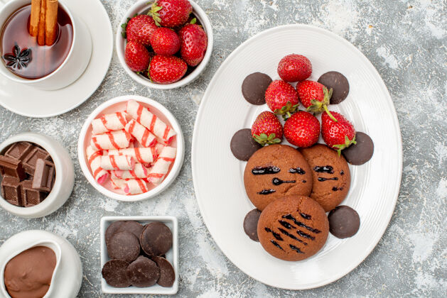 碗顶近距离观看饼干草莓和巧克力碗与可可糖草莓巧克力和茶与肉桂在灰白色的桌子上浆果糖果甜点