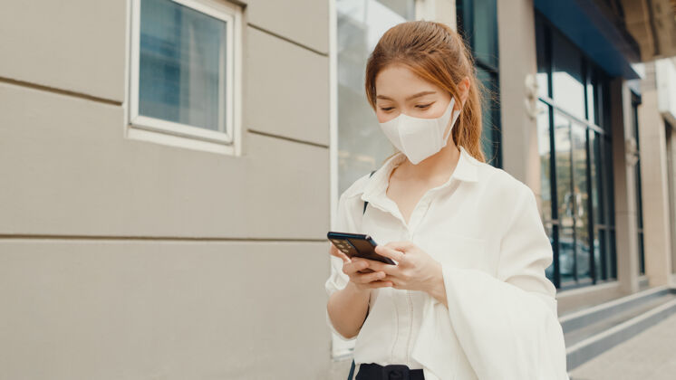 面具穿着时尚办公服 戴着医用面罩 使用智能手机的成功亚洲年轻女商人金融莫比尔病毒
