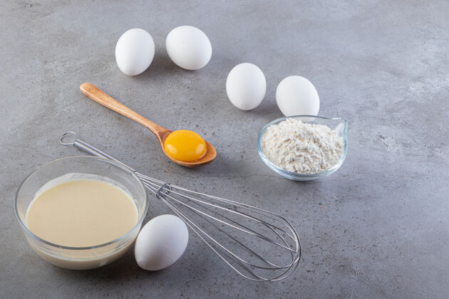 木头生的白鸡蛋和面粉和牛奶放在石桌上勺子食物蛋黄