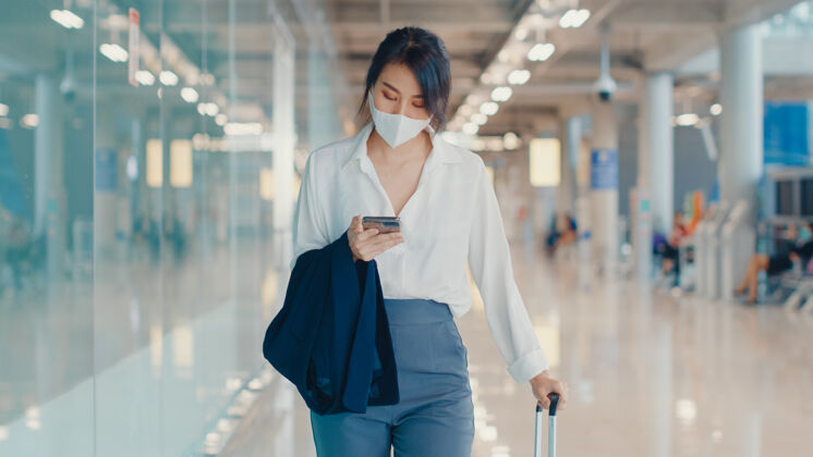 步行亚洲商务女孩用智能手机检查登机牌 带着行李到机场国内航班的候机楼漫游年轻人旅客
