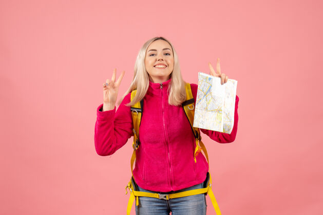 背包正面图微笑的女旅行者 背着黄色背包 拿着地图 示意胜利标志时尚手势胜利