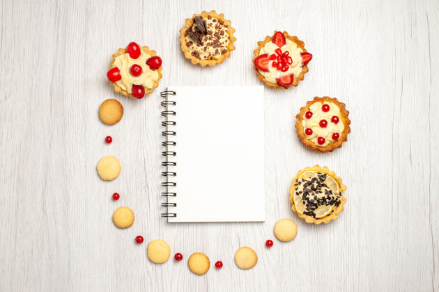 食物俯视图白色木质地面中央 一个被馅饼和饼干包围的笔记本中心形状框架