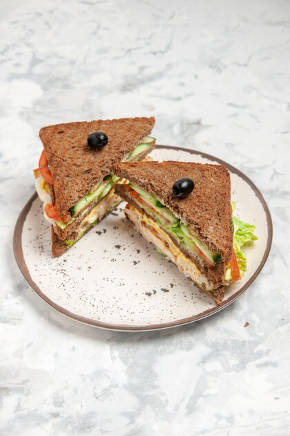 食物美味三明治的垂直视图 黑色面包上有橄榄装饰 盘子上有白色污渍美味烧烤肉