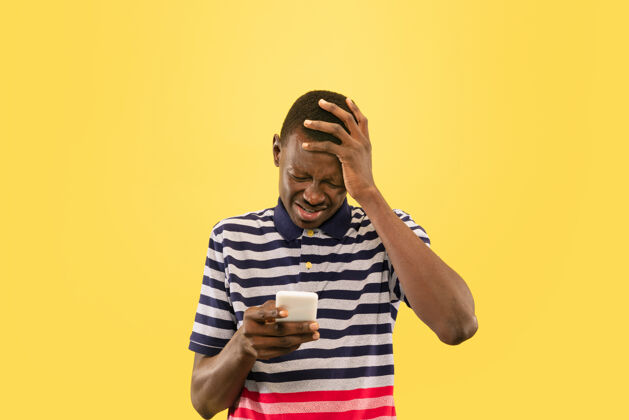 商人年轻的非洲裔美国男子用智能手机隔离在黄色的工作室背景下 面部表情美丽的男性半身肖像人类情感的概念 面部表情非洲人成功幸运