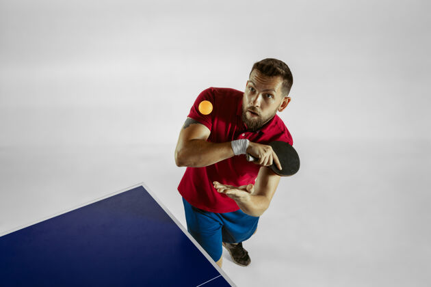 玩在白色工作室墙上打乒乓球的年轻人乒乓球运动员球拍
