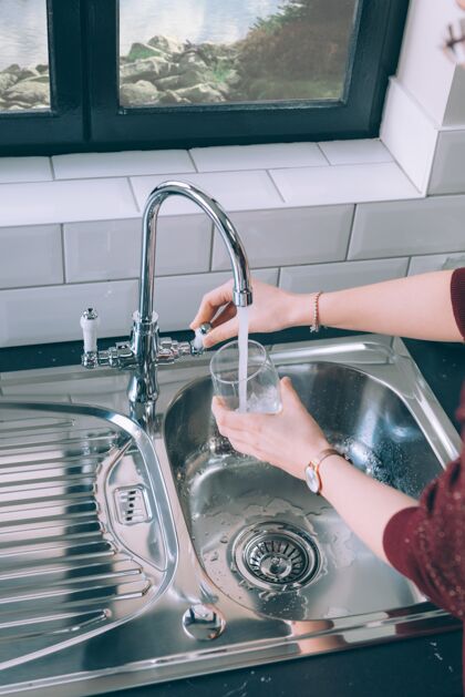 房子女人从厨房的钢制水龙头往杯子里灌水室内家庭洗