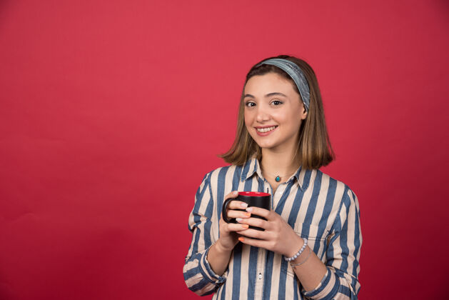 马克杯开朗的女人端着一杯咖啡 摆着姿势站在前面年轻快乐咖啡