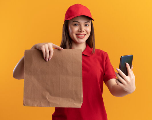 纸身着制服的微笑漂亮的送货员手里拿着橙色的纸包和电话送货女人制服