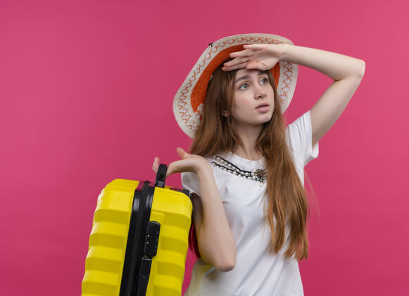 抱着焦急的年轻旅行家女孩戴着帽子拿着手提箱把手放在额头上遥望着孤立的粉色空间旅行者粉色戴着