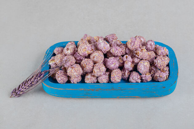 玉米紫色的麦秆靠在大理石桌上的一个木盘上 上面放着一盘蜜饯爆米花糖果爆米花谷物
