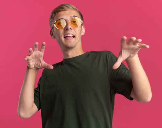 衬衫快乐的年轻帅哥穿着绿色衬衫 戴着眼镜 在粉红色的墙上显示出老虎式的手势市民快乐人