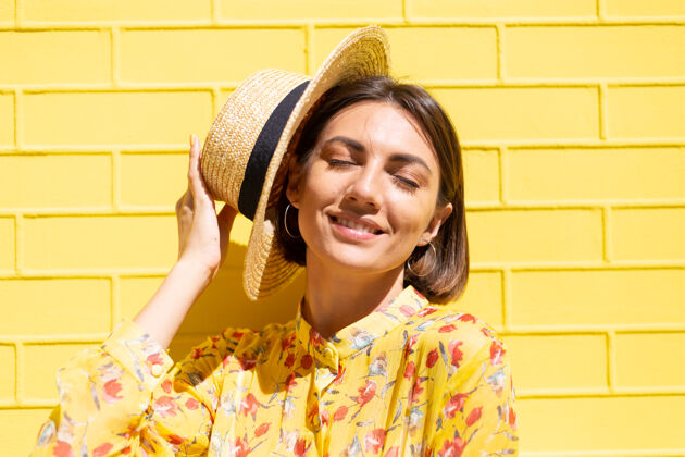 姿势黄砖墙上戴着黄色夏装和帽子的女人沉着而积极 享受着阳光明媚的夏日欢乐太阳城市