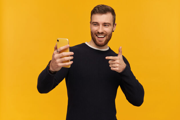 人物帅哥 黑发 胡须 穿黑色毛衣 自拍 视频通话 手指对着屏幕 看着手机 隔着黄色的墙颜色酷独身