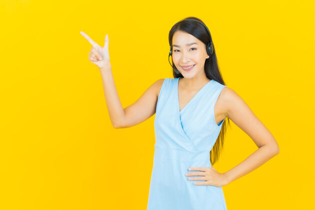 支持在黄色的墙上画上一幅美丽的亚洲年轻女子与呼叫中心客户服务中心经纪人运营商耳机