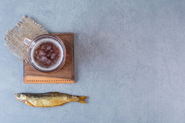 营养干咸鱼和啤酒杯放在大理石表面的木板上新鲜板冷