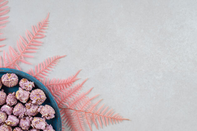 爆米花放在大理石桌上一束粉红色叶子上的一小盘涂着糖果的爆米花平铺复制空间垃圾食品
