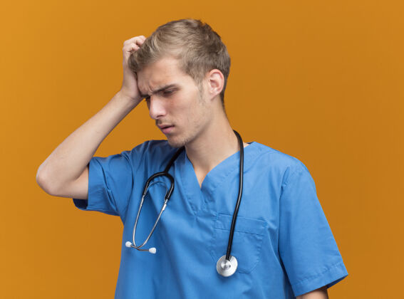 男性遗憾的是 年轻的男医生穿着医生制服 用听诊器在橘黄色的墙上划破了头姿势人公民
