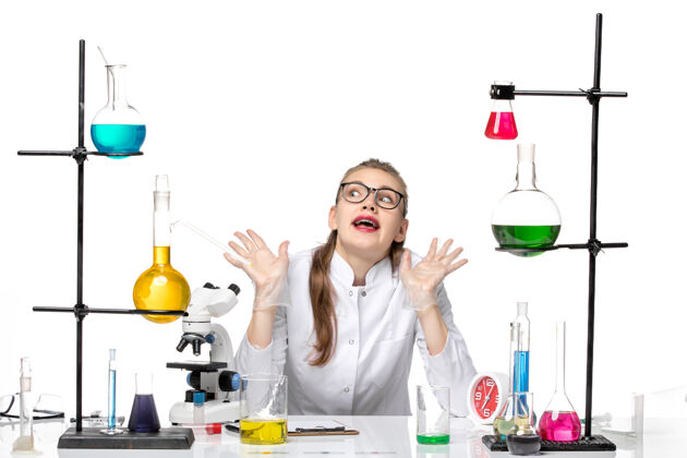 医学前视图：身着医疗服的女化学家坐在桌子前 在白色背景上拿着溶液大流行化学冠状病毒成人医学桌子