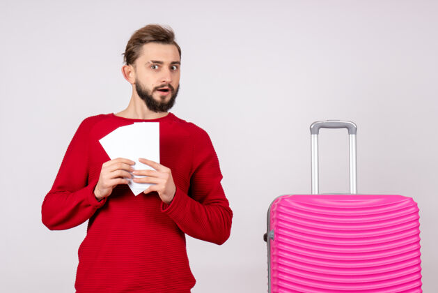 航班正面图：年轻男性 带着粉红色的包 手持白墙旅行的机票 彩色度假的航班 旅行的游客游客机票肖像