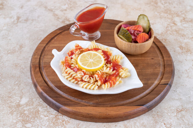 拼盘一盘煮熟的意大利面 番茄酱和一碗混合在大理石表面的泡菜黄瓜碗柠檬