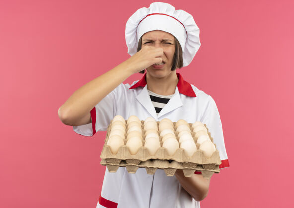 粉红色年轻的女厨师穿着厨师制服 手里拿着一盒鸡蛋 鼻子被粉红色隔离开来鸡蛋烹饪鼻子