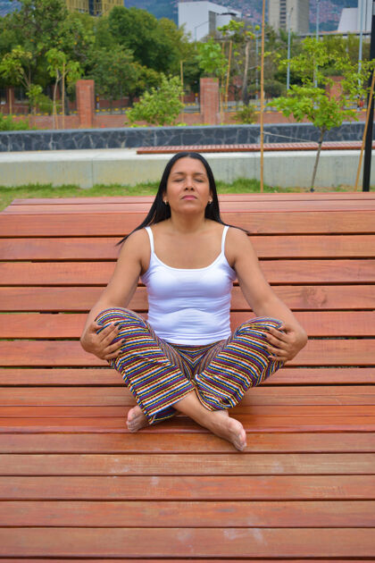 垂直一位拉丁女性在公园的木凳上冥想的垂直镜头阳光自然木头