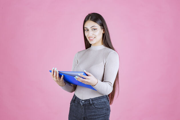 人类女孩拿着一个蓝色的项目文件夹 看起来很成功和快乐幸运清单姿势