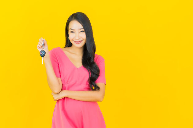 亚洲画像美丽的亚洲年轻女子微笑着把车钥匙放在黄色的墙上旅游显示业主