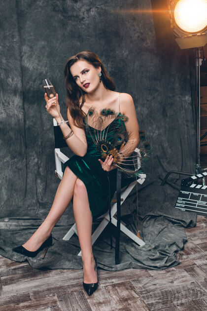 漂亮年轻时尚性感的女人坐在电影院后台的椅子上 用一杯香槟庆祝微笑女士波基
