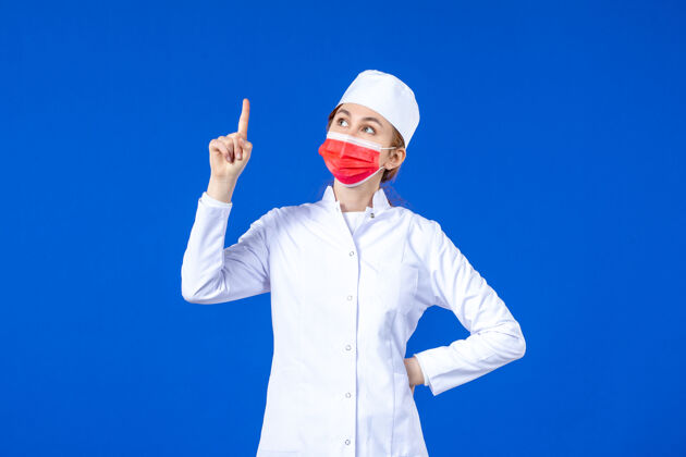 正面正面图身着医疗服的年轻护士 蓝色墙上戴着红色防护面具疾病药品防护
