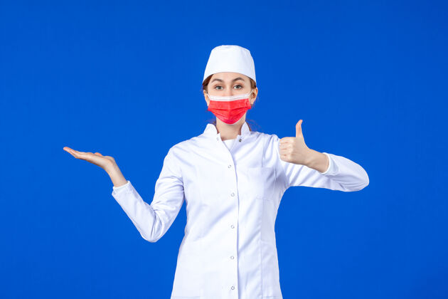 口罩正面图身着医疗服的年轻护士 蓝色墙上戴着红色防护面具成人大流行蓝色