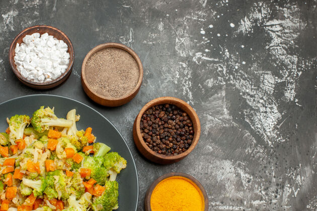 料理健康餐 黑盘子上放花椰菜和胡萝卜 灰色桌子上放香料胡萝卜蔬菜碗