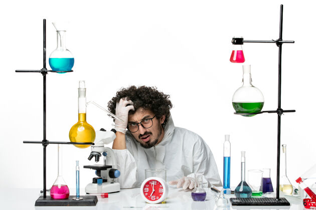 特殊正面图穿着白色特别套装的年轻男科学家坐在那里 拿着解决方案化学实验室烧杯