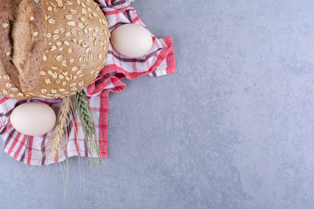 小麦把麦秆 鸡蛋和一条面包放在大理石表面的毛巾上烘焙食品面包皮谷物