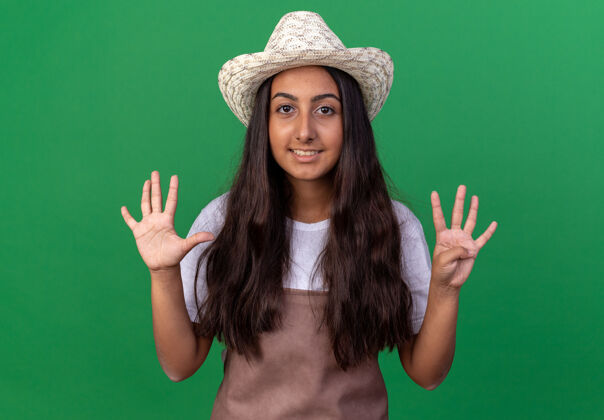 围裙穿着围裙 戴着夏帽的年轻园丁女孩微笑着站在绿墙上的九号人物年轻的帽子表演