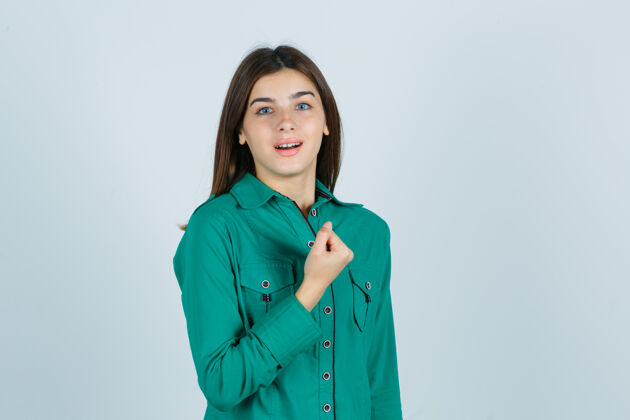 胸部穿着绿色上衣的年轻女孩握紧拳头放在胸前 看上去很欢快正面视图年轻衬衫年轻