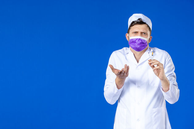男医生身穿医疗服 戴着紫色口罩的男医生正对着蓝色的脸拿着针剂领结药品药品