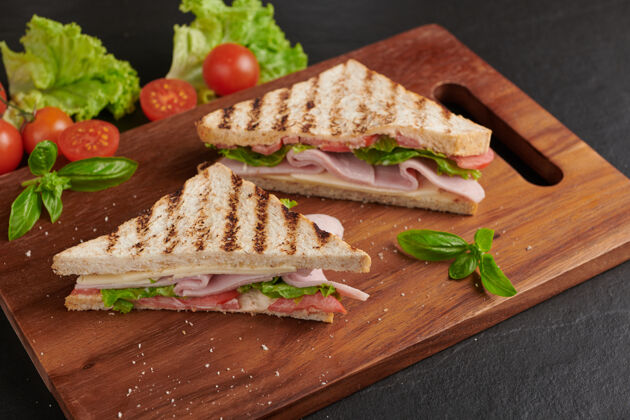 美味烤三明治配火腿 奶酪 西红柿和生菜 放在木制砧板上火腿美味午餐