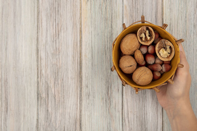 食物女性手拿着一桶不同坚果的顶视图 比如核桃和榛子 放在一个灰色的木质表面上 上面有复制空间坚果美味顶视图
