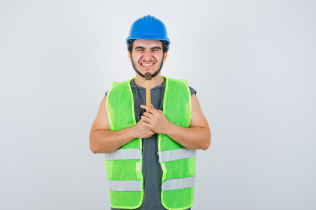 人年轻的建筑工人穿着工装 下巴下拿着锤子 看上去很快乐 正对着窗外肖像胡须男性