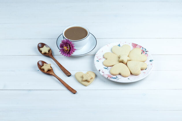 小吃一些心形和星形的饼干和花 饼干放在木勺里 一杯咖啡放在白色木板背景上的白色盘子里 高角度观看饼干薯条新鲜