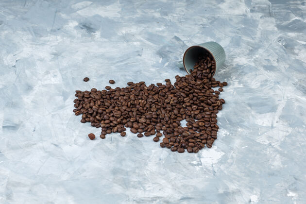 高从灰色灰泥背景上的杯子中高角度观察散落的咖啡豆水平食物阿拉比卡谷物