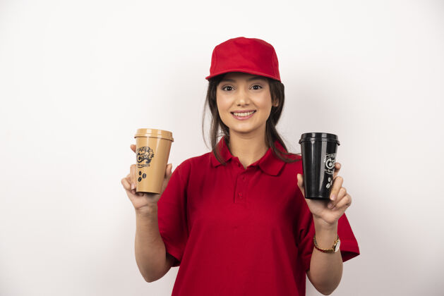人送货员戴红帽的女人拿着白色背景的咖啡杯承运人女咖啡