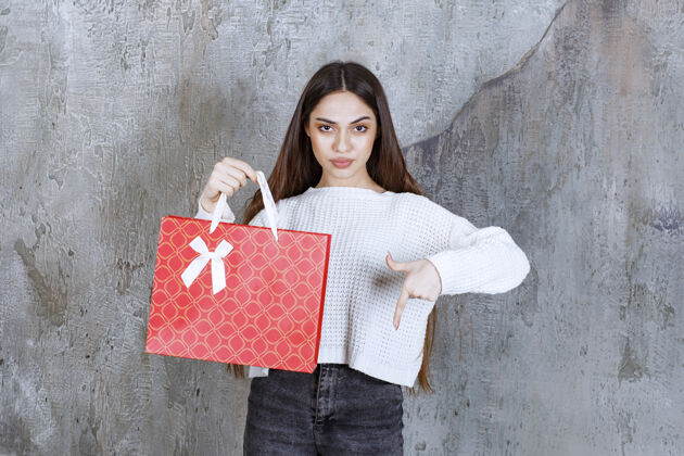 介绍穿白衬衫的女孩拿着一个红色购物袋 邀请旁边的人送礼物成人快递女售货员
