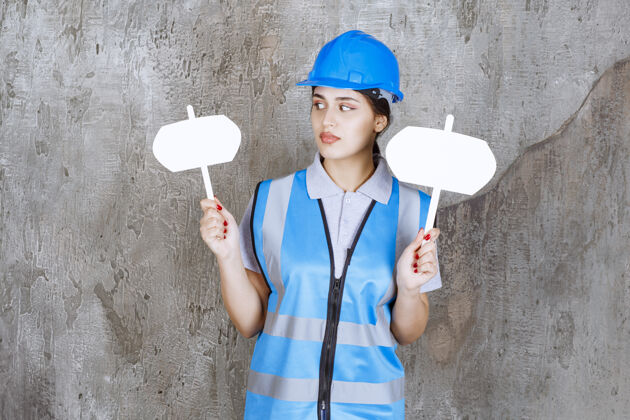 亮点身穿蓝色制服 头戴安全帽的女工程师 双手拿着两块空白的信息板年轻人年轻人位置