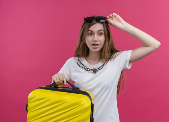 手提箱惊讶的年轻旅游女孩头戴太阳镜拿着手提箱 手戴太阳镜在孤立的粉红色墙上女人戴着拿着