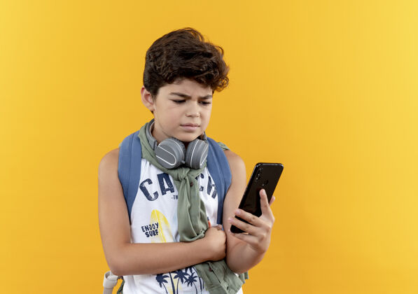 电话想着那个背着书包戴着耳机的小男孩 手里拿着手机 看着隔离在黄色墙上的电话小学校背