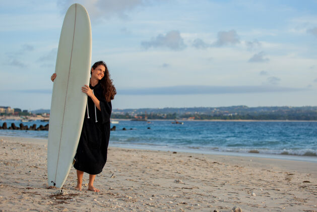 海滩运动美丽的女孩拿着冲浪板站在沙滩上运动女性人